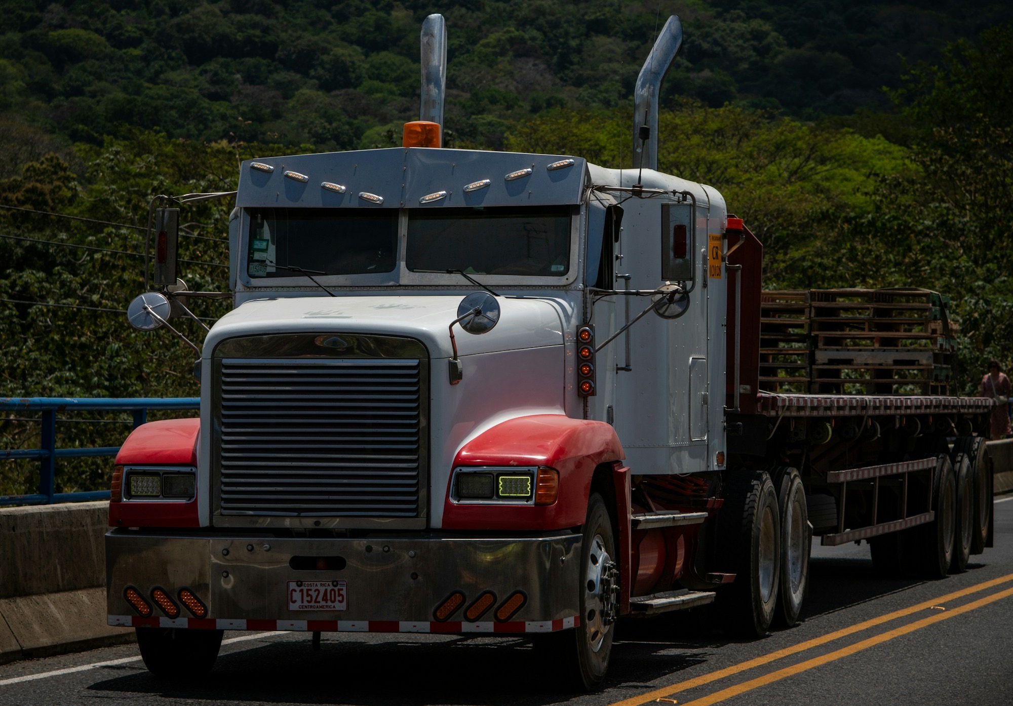 White and red long-nose semi pulling an empty flatbed trailer on a highway
